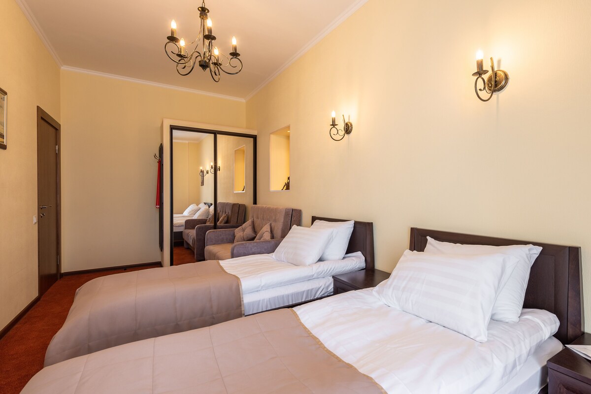 A hotel room with two beds, a chandelier, wall sconces, a mirror, and a door.