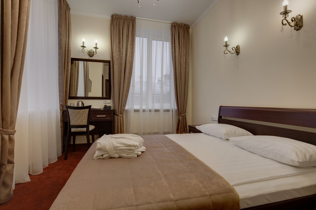 A hotel room with a large bed, a desk with a chair, a mirror, and two wall sconces.