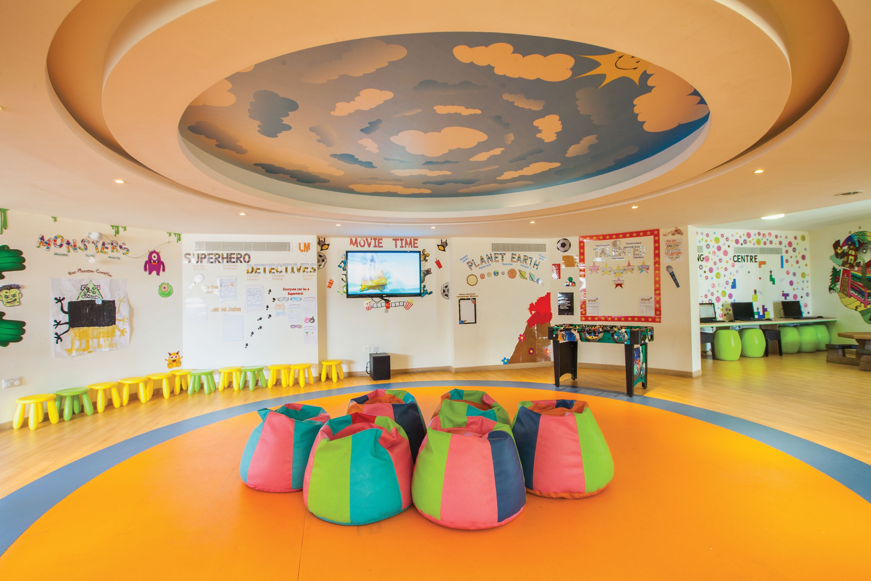 Ein helles Zimmer mit bunten Sitzsäcken, einem Fernsehbildschirm und lehrreichen Postern an den Wänden.