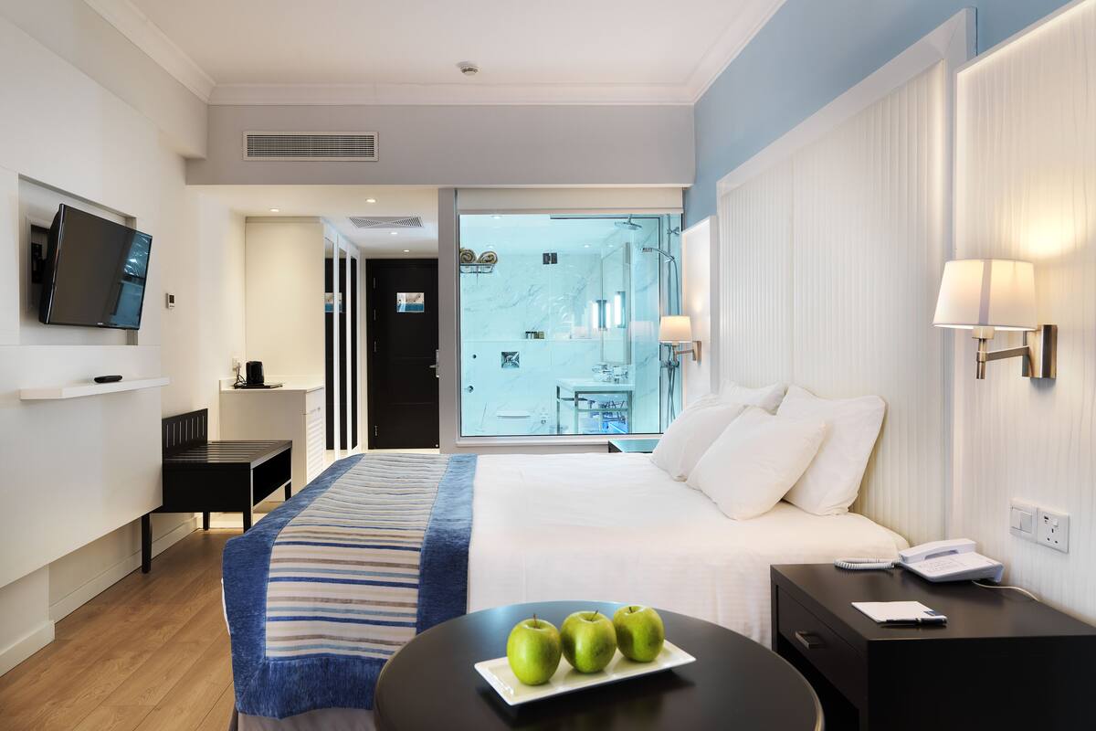 Moderni hotellihuone, jossa on sänky, yöpöytä, lamppu ja näkymä kylpyhuoneeseen.