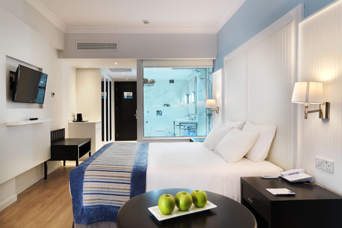 A modern hotel room with a bed, bedside table, lamp, and a view of the bathroom.
