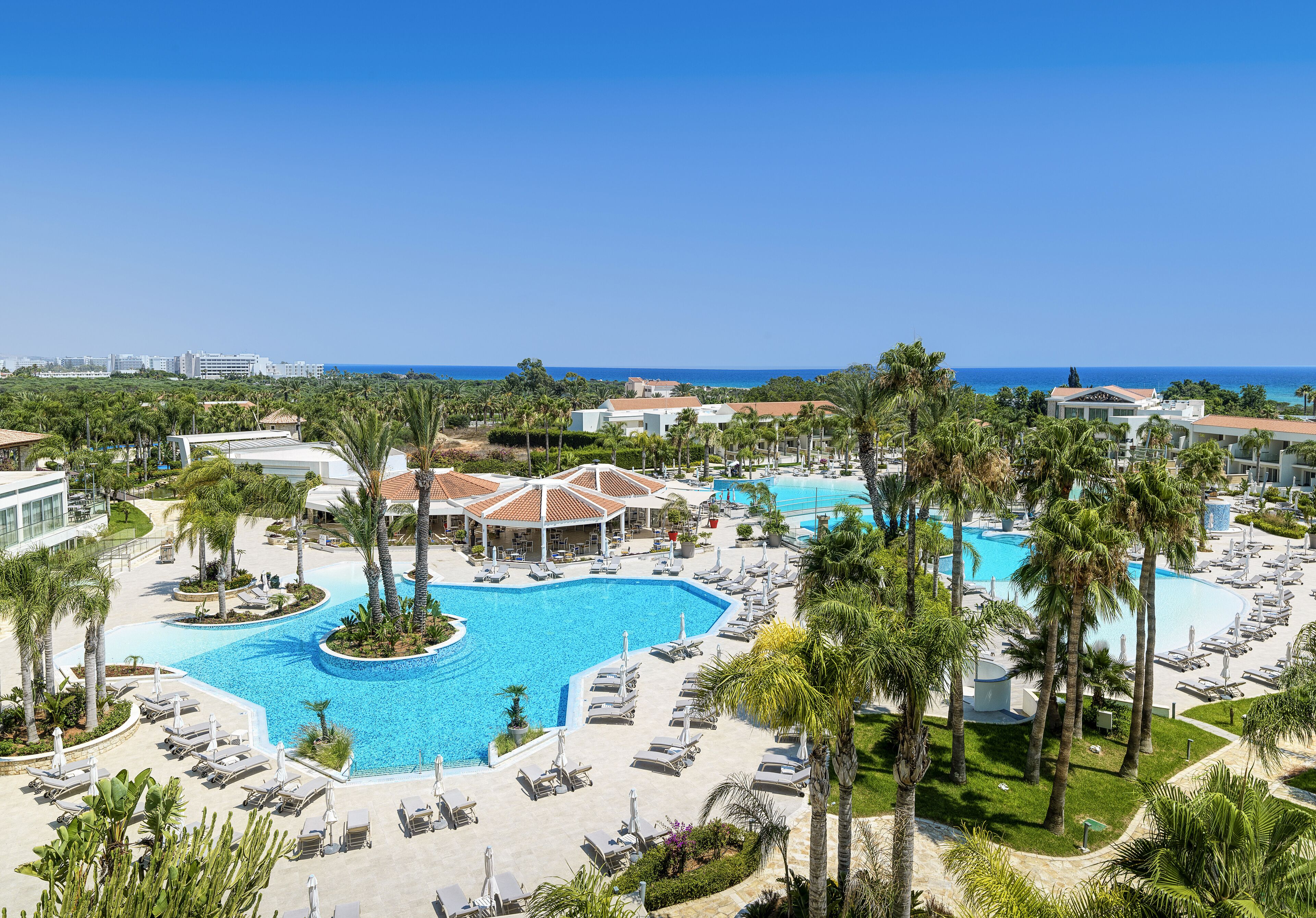 A resort with multiple swimming pools, palm trees, and a view of the ocean.