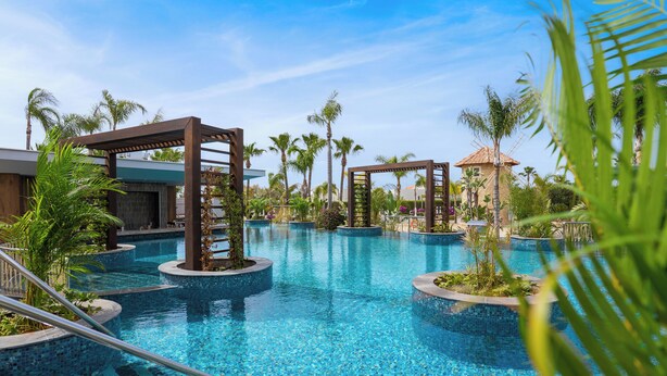 A pool area with multiple circular pools, palm trees, and a wooden pergola structure. - Olympic Lagoon Resort – Ayia Napa (Ayia Napa)