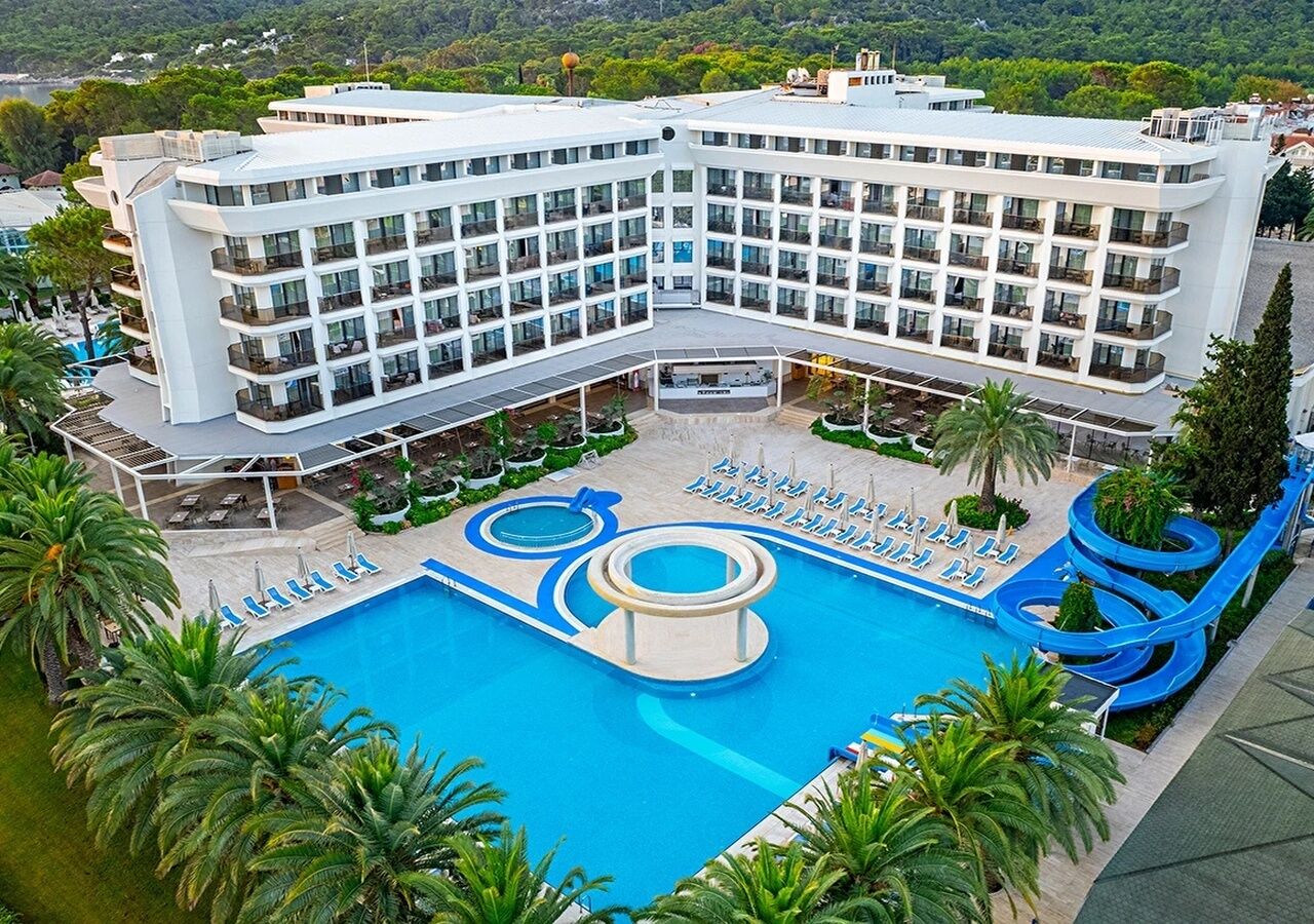 Un hotel con una amplia piscina de diseño circular, rodeado de palmeras y un tobogán de agua.