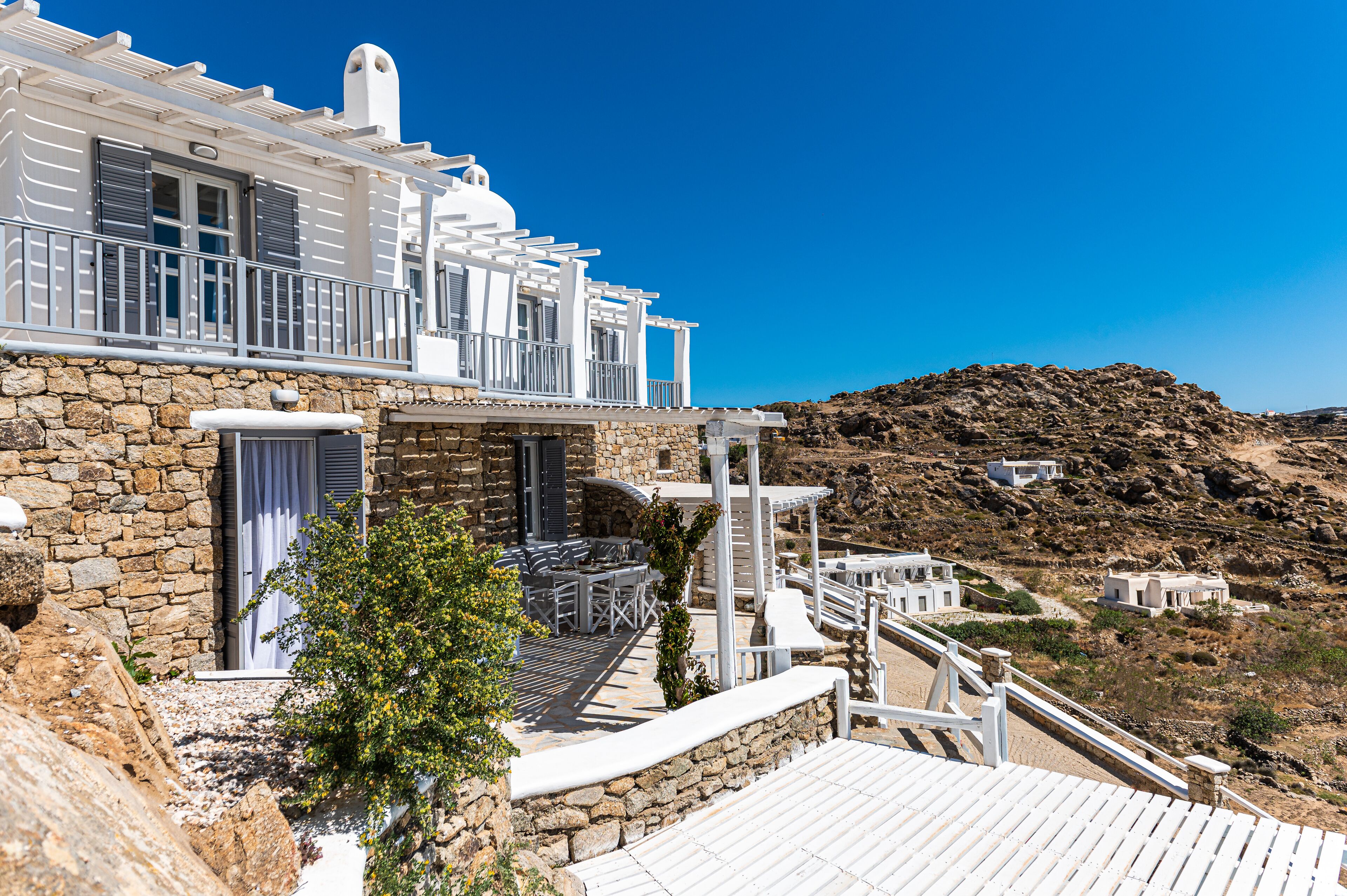 Un edificio blanco con muros de piedra, un balcón y mesas al aire libre.