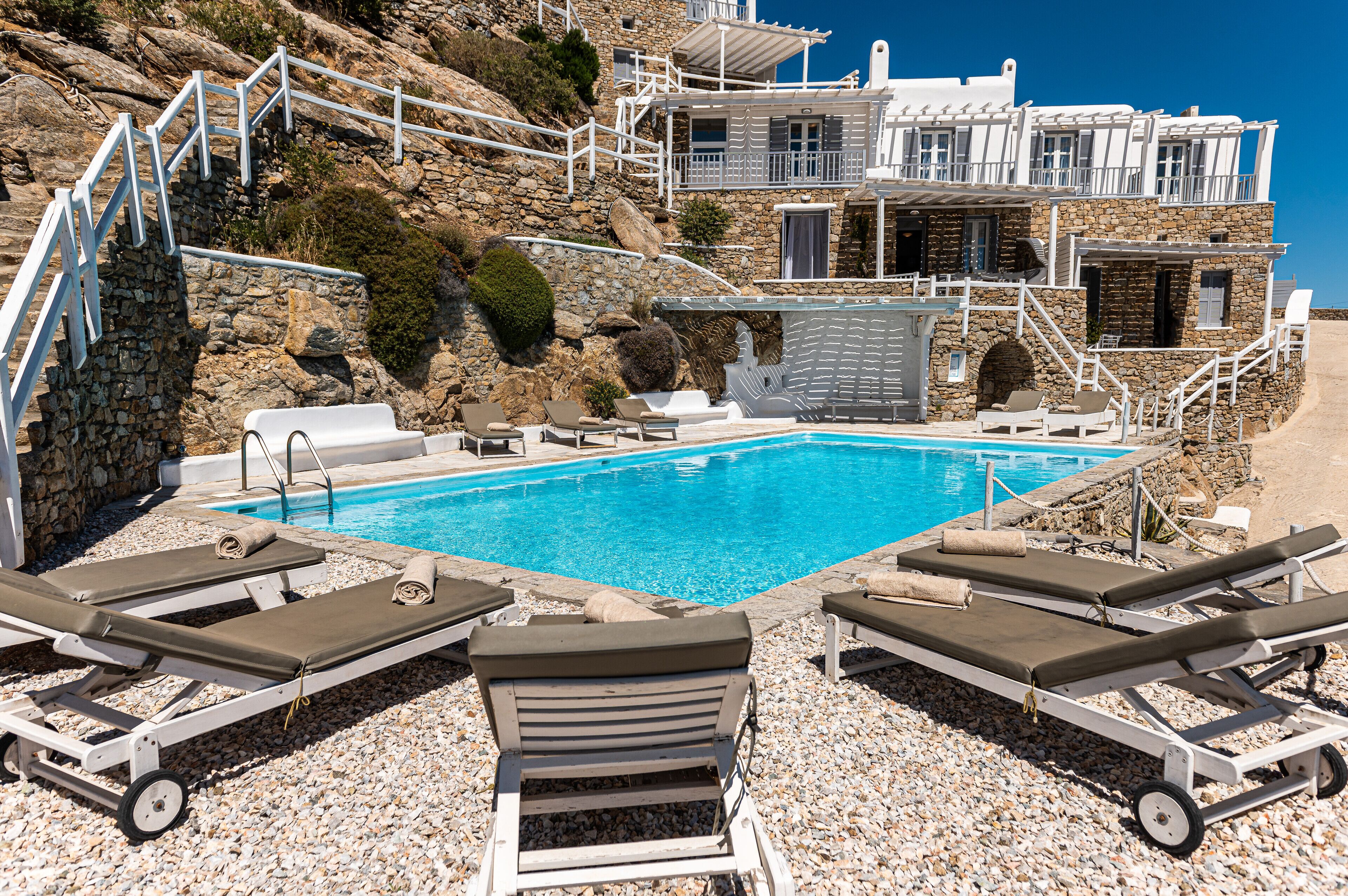 A poolside area with lounge chairs, a clear blue pool, and a stone building with a balcony.