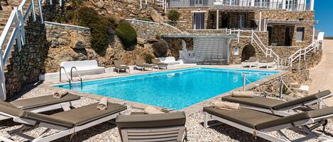 A poolside area with lounge chairs, a clear blue pool, and a stone building with a balcony.