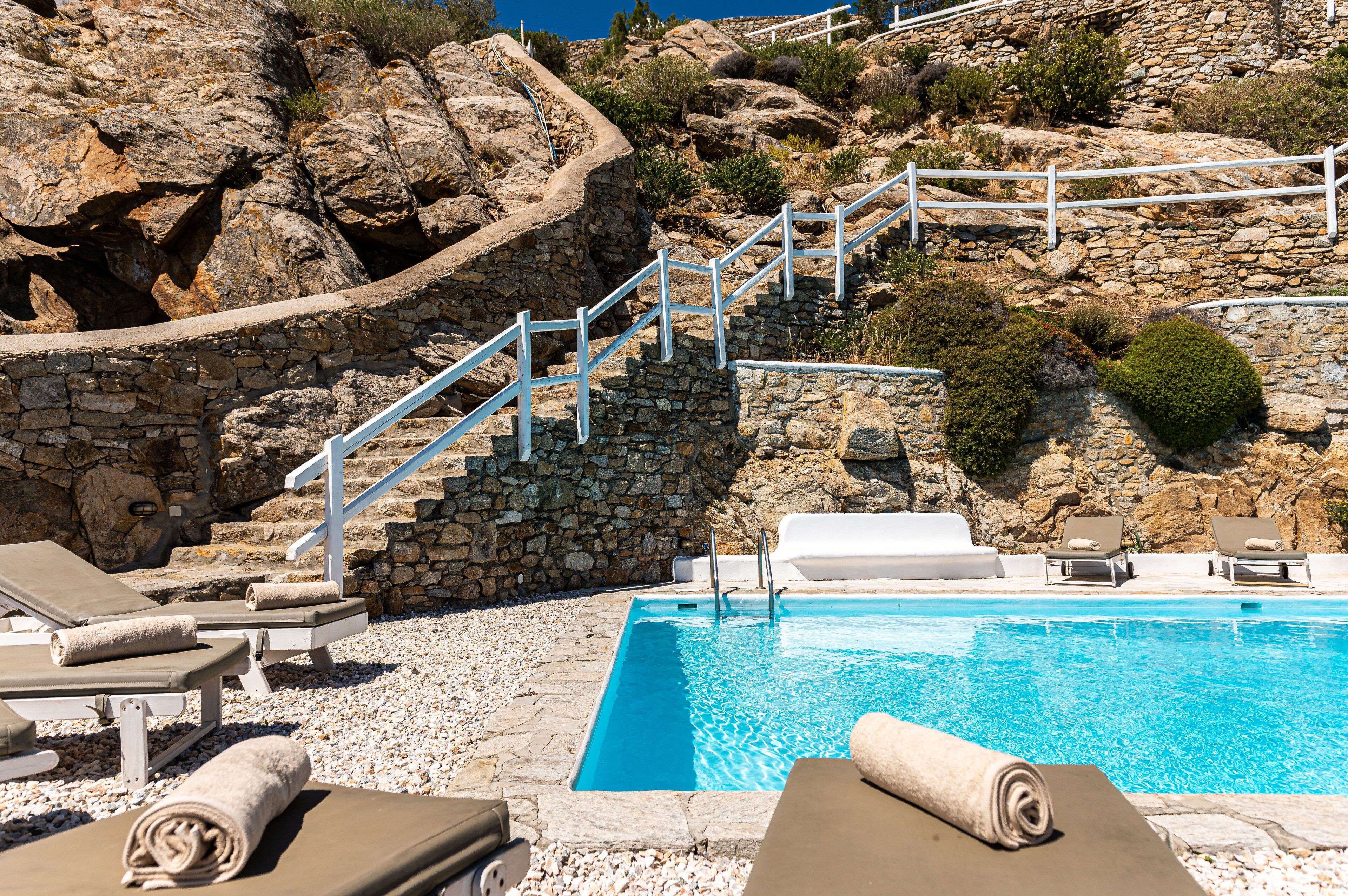 Una piscina de piedra con barandillas blancas y sillas de descanso.