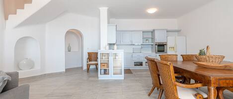 A spacious living area with a dining table, chairs, and a kitchen in the background.