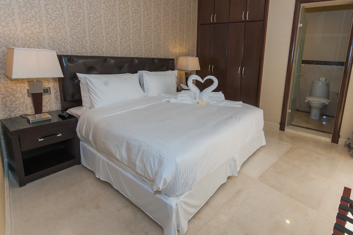 A neatly made bed with white linens, a dark headboard, and two bedside lamps.