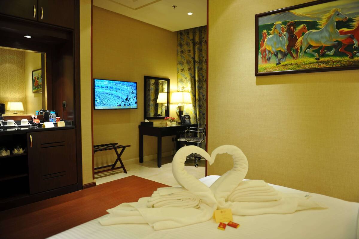 A hotel room with a bed, a TV, a desk, and a swan-shaped towel arrangement.