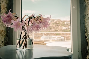 Um vaso com flores cor-de-rosa sobre uma mesa, próximo a uma janela com vista para a paisagem costeira.