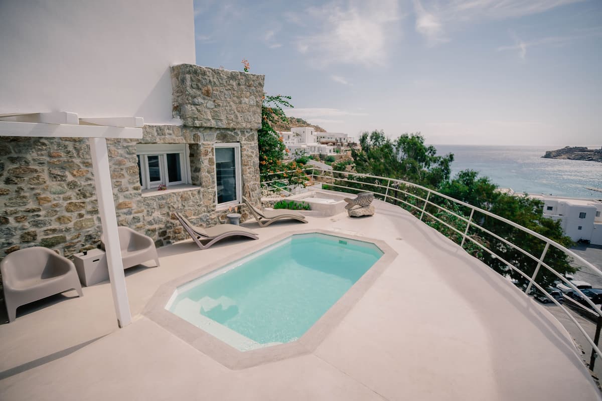 Zona de piscina en la azotea con paredes de piedra, sillones de descanso y vistas al mar.