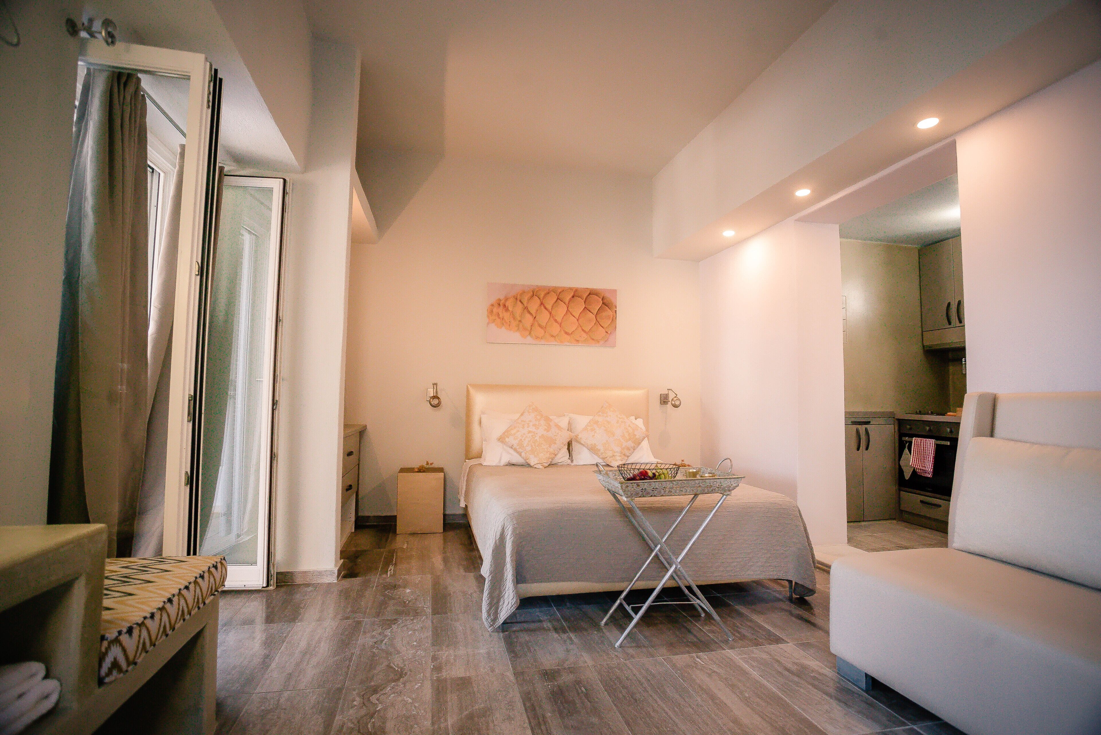 A bedroom with a bed, bedside table, and a small table with a basket. There is a bathroom with a shower curtain and a toilet. The room has a modern design with a light color scheme.