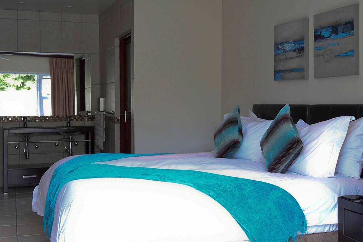 A modern bedroom with a large bed, a bathroom with a vanity, and artwork on the walls.