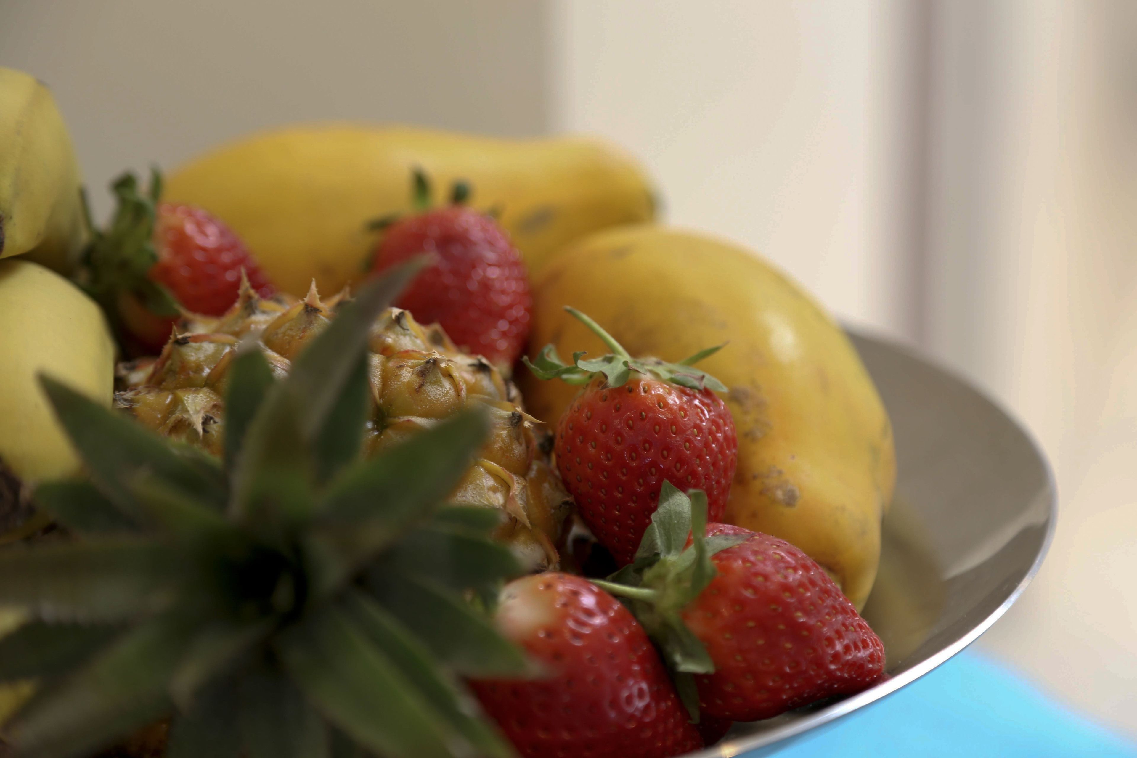A plate with a pineapple, strawberries, and bananas.