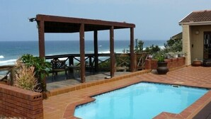 Una piscina con un toldo de madera, paredes de ladrillo y plantas en macetas.