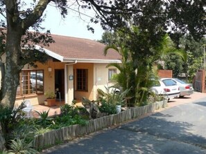 A single-story house with a tiled roof, a front porch, and a car parked in the driveway.