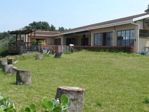 A single-story house with a large front porch, a covered outdoor area, and a well-maintained lawn with several tree stumps.