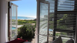 Ein Zimmer mit Blick auf Strand und Pool durch halb geöffneten Jalousien.