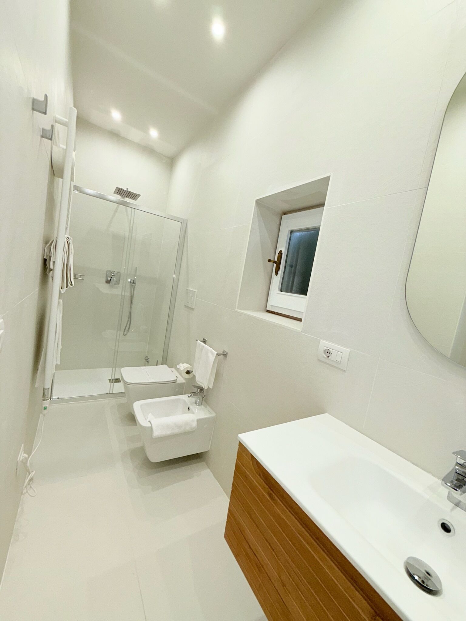 A modern bathroom with a glass-enclosed shower, a wooden vanity, and a large mirror.