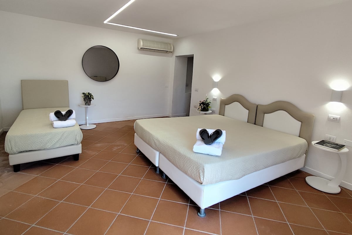 Une chambre d’hôtel avec deux lits, un miroir rond, un appareil de climatisation et une table de chevet avec un livre.