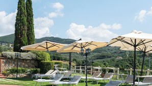 Una piscina con lettini e ombrelloni, immersa nel verde e circondata da colline.