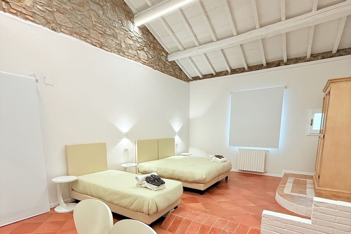 Une chambre avec deux lits, des murs blancs, un mur en pierre, un radiateur et une armoire en bois.