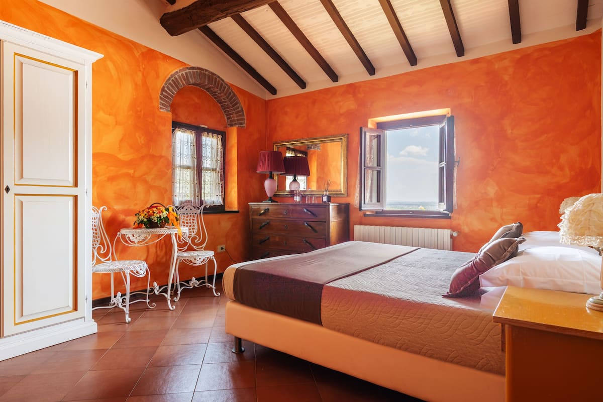 Une chambre à coucher comprenant un lit, une commode, une chaise, une table et une fenêtre donnant sur un beau paysage.