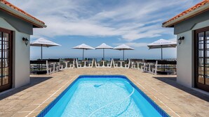 A swimming pool with a view of the sea, surrounded by umbrellas and chairs.