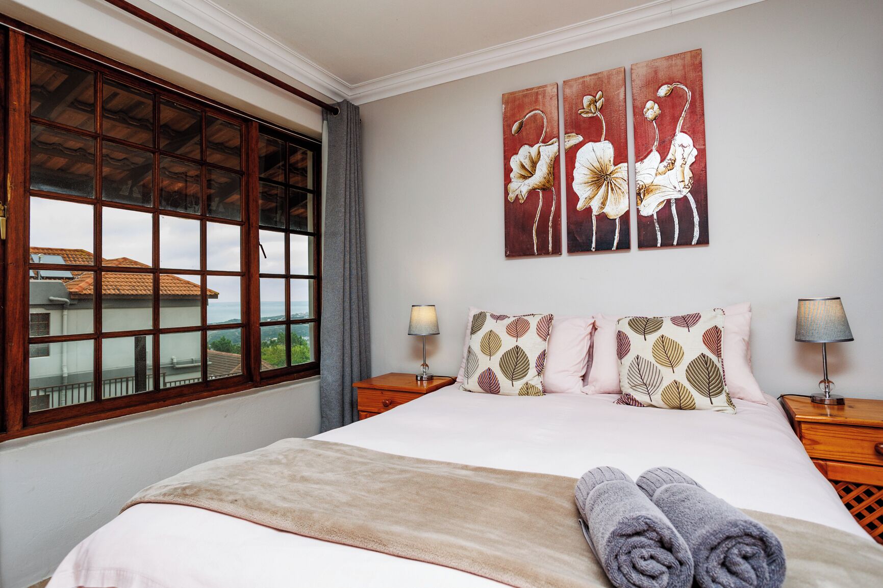 A bedroom with a large bed, two bedside tables, a window with a view, and a wall with three paintings.