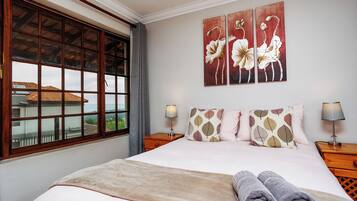A bedroom with a large bed, two bedside tables, a window with a view, and a wall with three paintings.