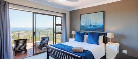 A bedroom with a bed, a painting, a ceiling fan, and a view through the glass door.