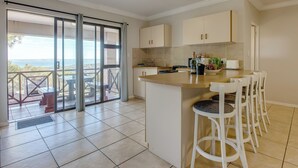 A kitchen with a bar area, sliding glass doors to a balcony, and a view of the sea.