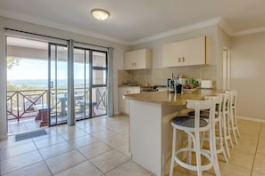 A kitchen with a bar area, sliding glass doors to a balcony, and a view of the sea. - Ilita Lodge (Great Brak River)
