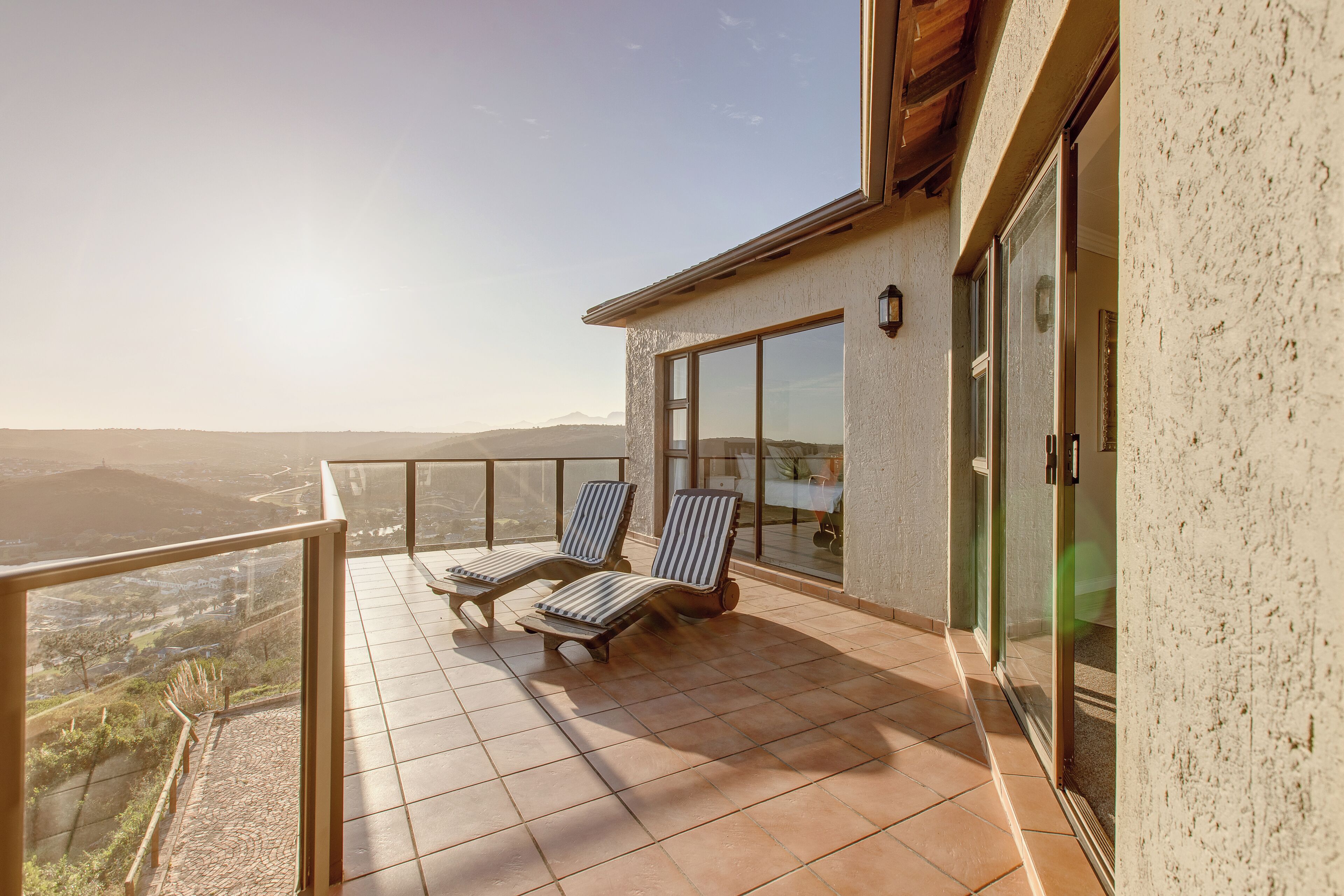 A balcony with two lounge chairs, a glass door, and a view of the landscape.