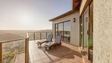 A balcony with two lounge chairs, a glass door, and a view of the landscape.