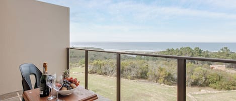 Un balcon avec une table dressée pour deux personnes, offrant une vue sur un paysage côtier.
