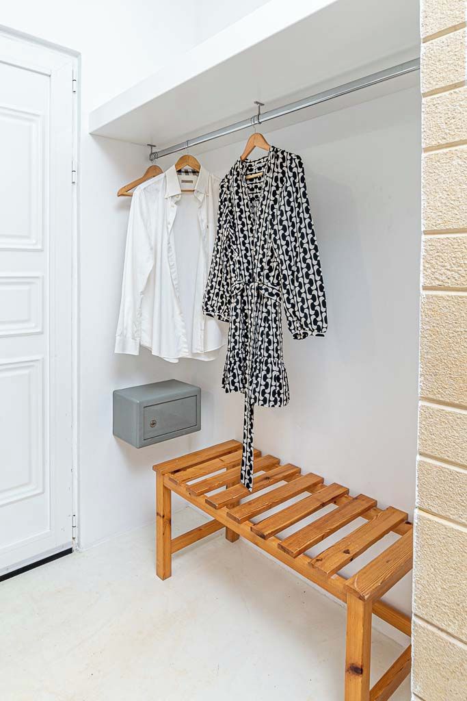 Een houten bank met metalen frame, een witte deur en een wandplank met een grijs object.