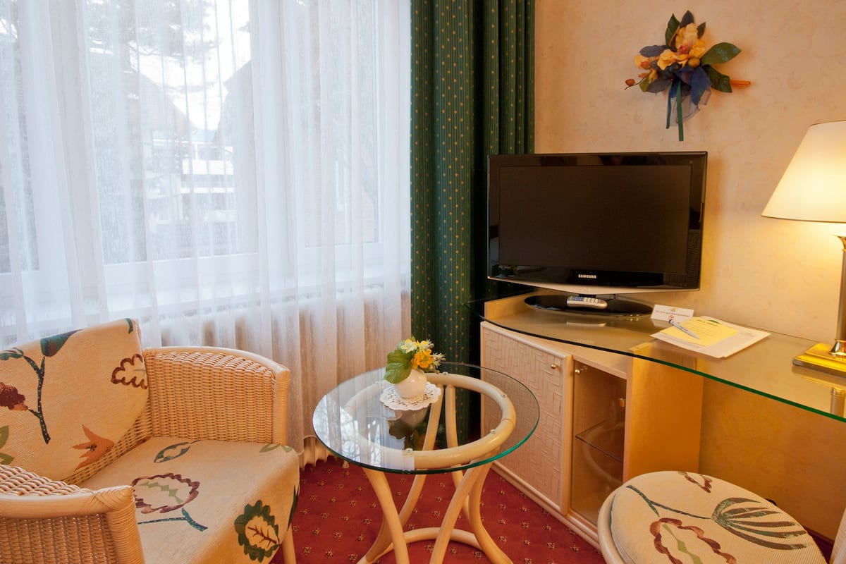 A hotel room with a television, a glass table, a sofa, and a small round table with a vase of flowers.