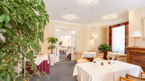 A hotel dining area with tables, chairs, potted plants, and a view into the dining room. - Park-Hotel Timmendorfer Strand (Timmendorfer Strand)
