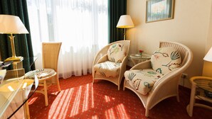 A hotel room with wicker furniture, a red carpet, and a large window with curtains. - Park-Hotel Timmendorfer Strand (Timmendorfer Strand)