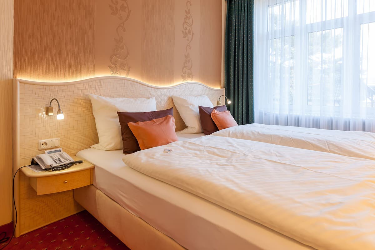 A hotel room with a large bed, a bedside table with a phone, and a wall with a decorative pattern.