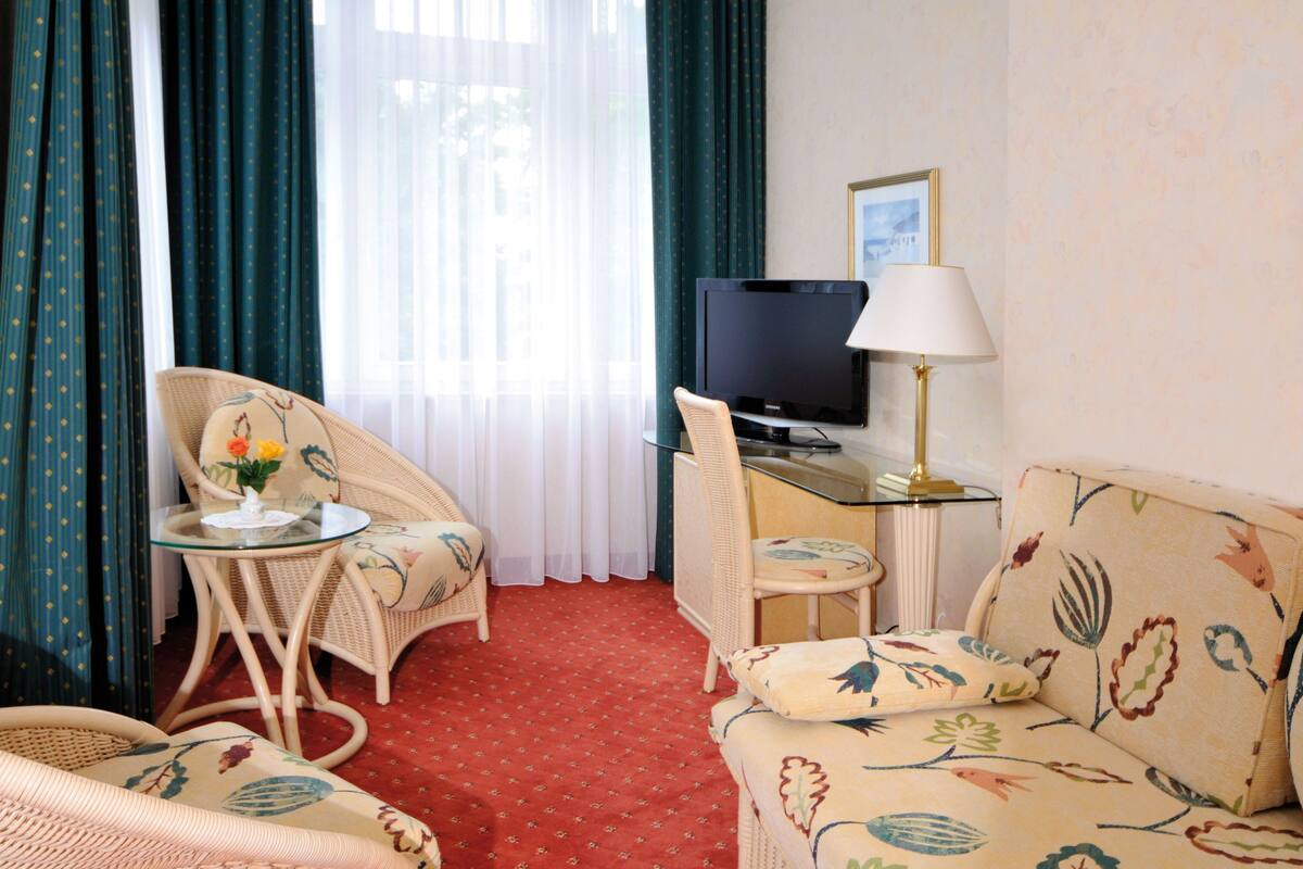 A hotel room with a red carpet, wicker furniture, a television, and a lamp.