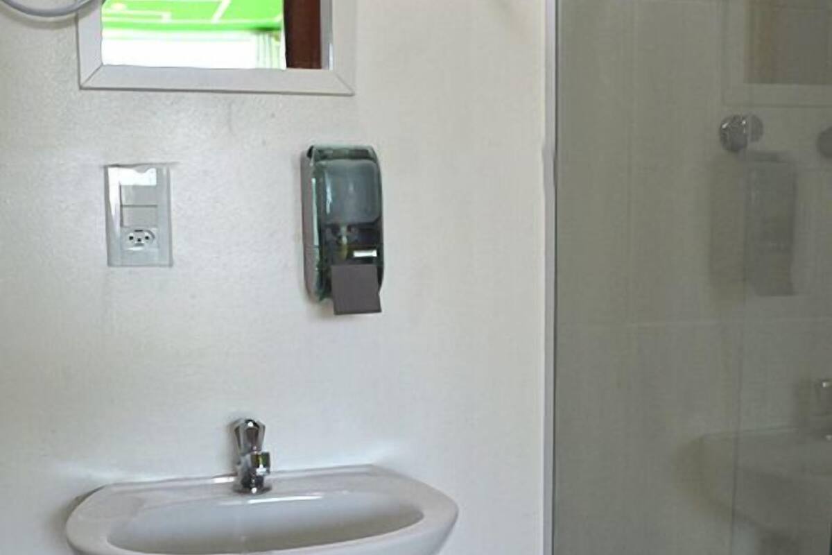 A bathroom with a white sink, a mirror, a soap dispenser, and a glass shower door.