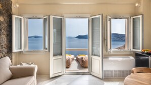 A room with a large bay window, a sofa, a small table, and a view of the sea. - Armeni Luxury Villas (Santorini)