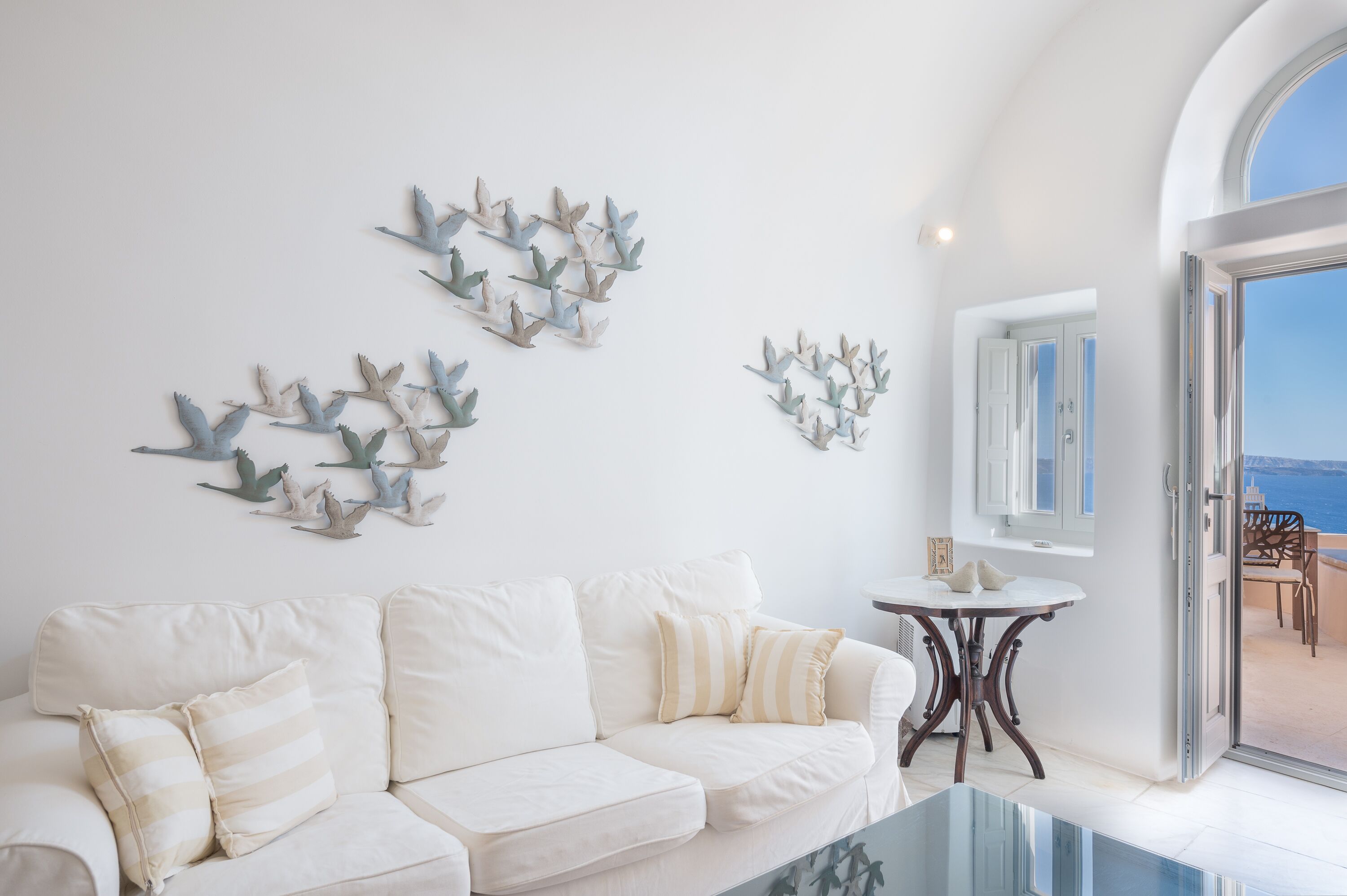 Una sala de estar blanca con un sofá blanco, una mesa de centro de vidrio y decoración en la pared.
