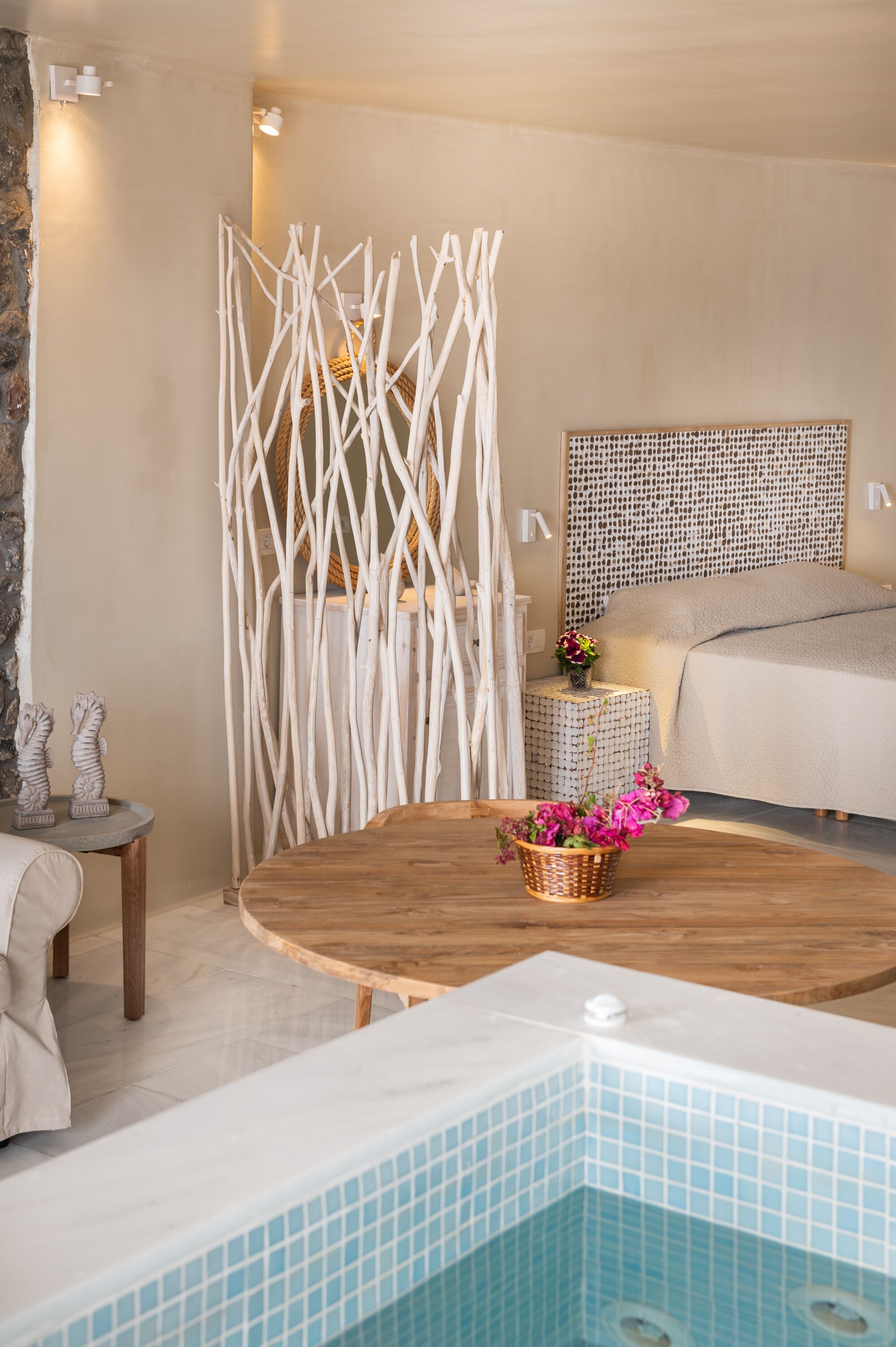 A modern bedroom with a large bed, a wooden coffee table, a small round table, and a decorative wall piece.