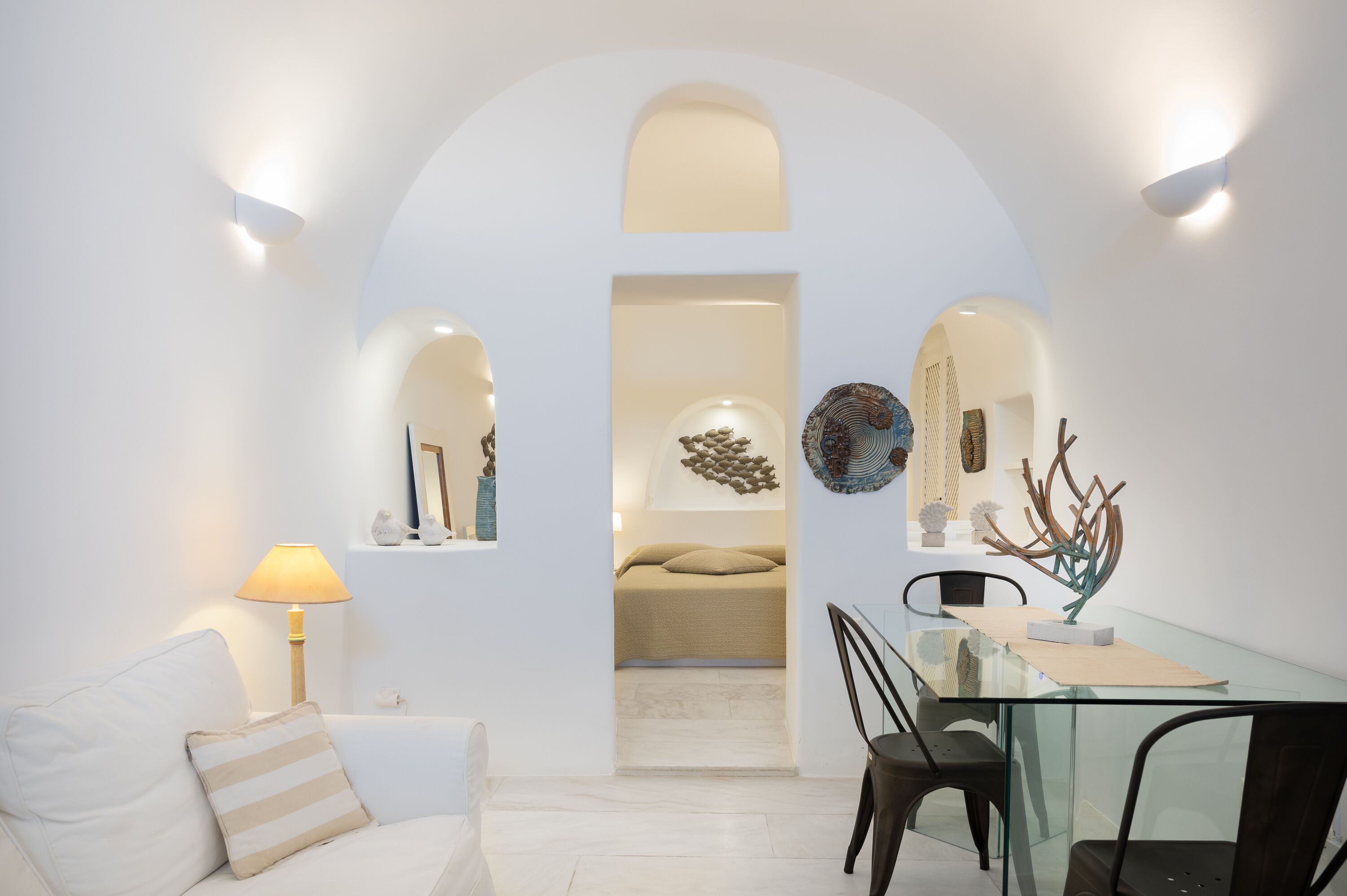 A modern interior with a glass dining table, white walls, and a cozy seating area with a lamp.