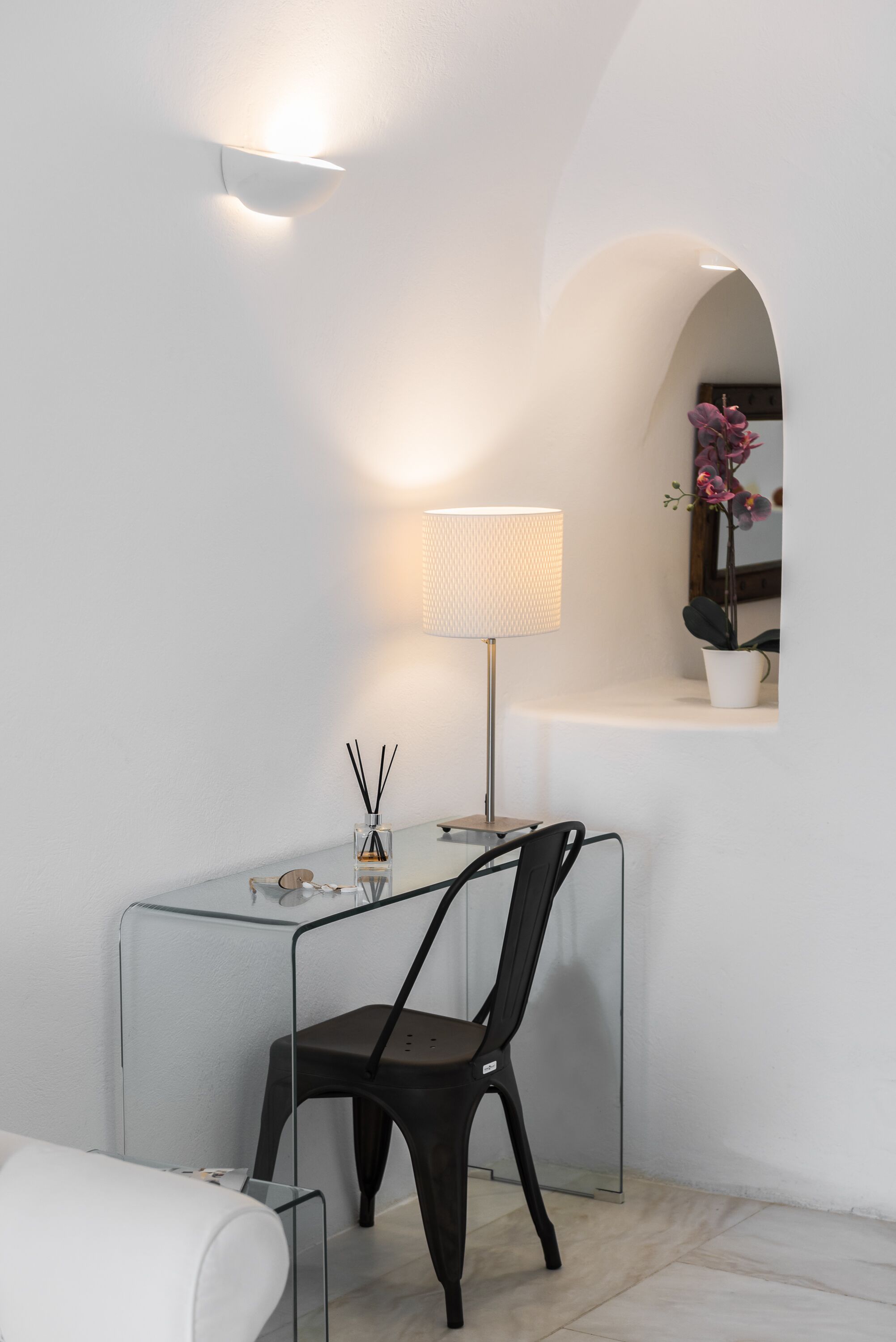 A modern, minimalist room with a glass desk, a black chair, a lamp, and a small potted plant.